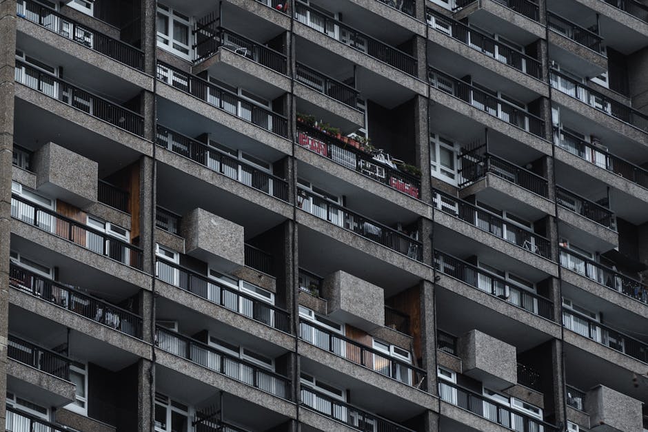 Photograph of an apartment building facade with multiple balconies and windows. The building features pink and cream-colored exterior walls, with some sections having brickwork detail. Several balconi